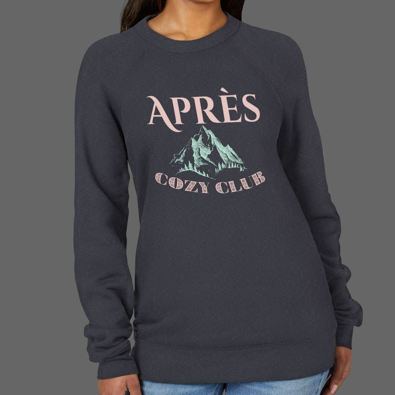 Woman wearing a dark gray sweatshirt with 'APRèS COZY CLUB' text and mountain graphic on a white background