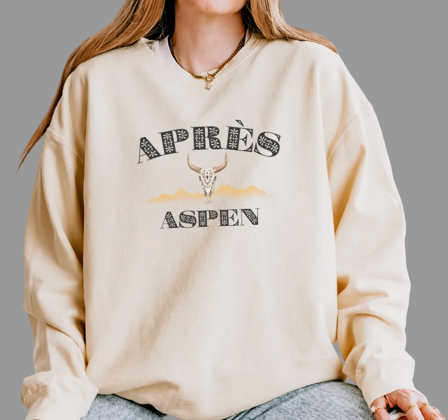 Beige sweatshirt with 'Apres Aspen' text and graphic on a plain background