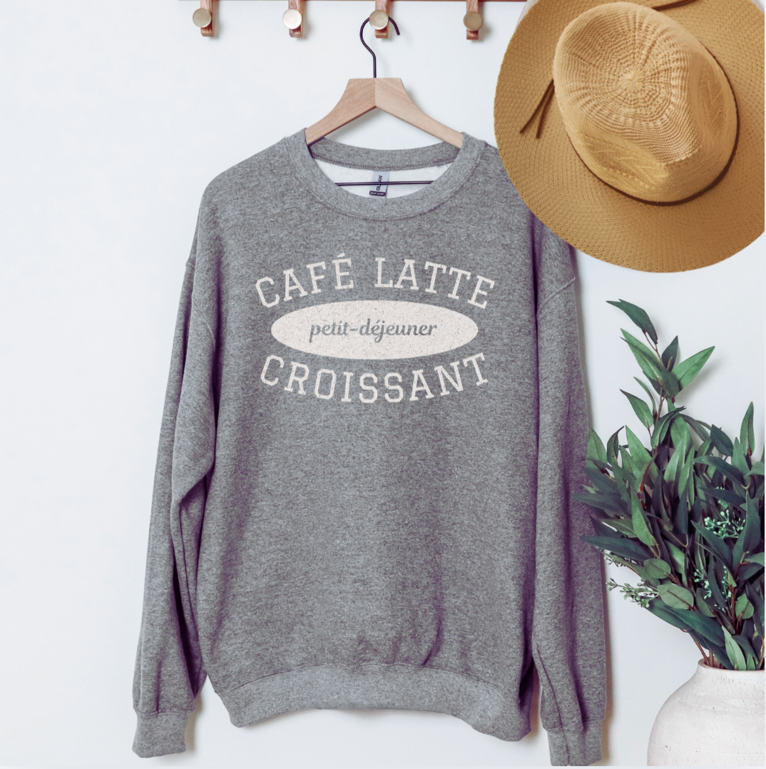 Gray sweatshirt with text on a hanger next to a straw hat and plant