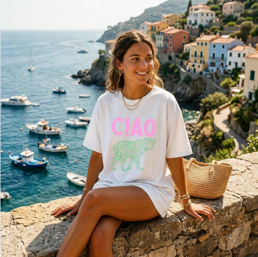Woman sitting on a stone wall overlooking a coastal town with boats and buildings.